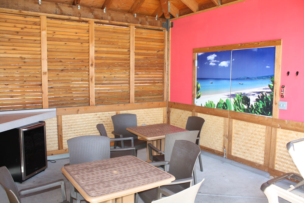 Inside view of a cabana at thunder bay with two tables, eight chairs and a fridge